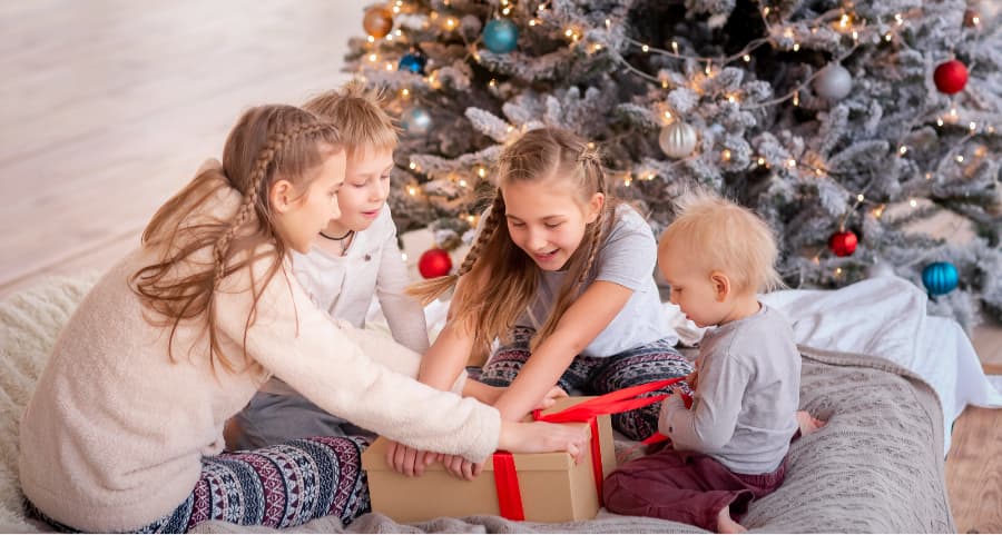 Siblings opening a present next to a Christmas tree.